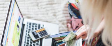 Woman pulling cash out of her wallet next to a laptop and phone