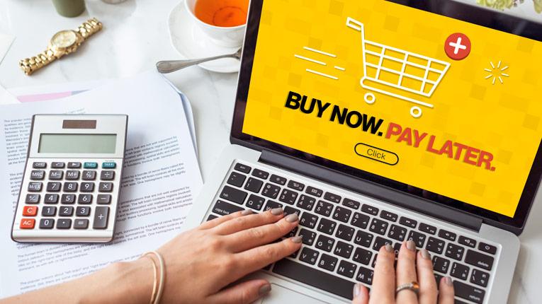 Woman's hands on keyboard of laptop displaying image of shopping cart and buy now, pay later text