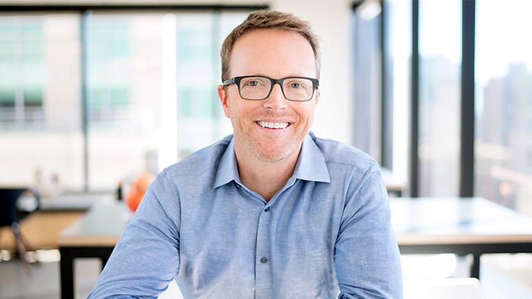 Man in blue button up shirt and glasses smiling